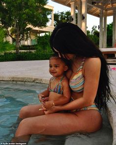 a woman holding a baby in her lap while sitting on the edge of a pool