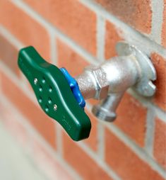 a water faucet attached to a brick wall with a green spigot on it