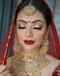 a woman wearing a red and gold bridal outfit with jewelry on her head,