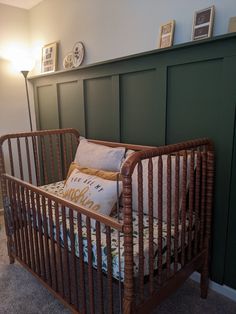 a baby crib in a room with green paneling and pictures on the wall