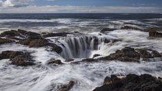 a black and white photo of waves crashing on rocks in the ocean under a cloudy sky