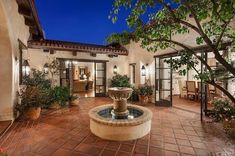 a courtyard with a fountain and potted plants in it at night or day time