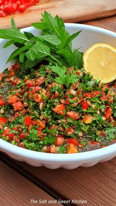 a white bowl filled with lots of food on top of a wooden table next to a cutting board