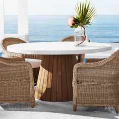 there is a table and chairs on the patio by the ocean with flowers in a vase