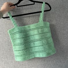 a crocheted bag hanging on a hanger with someone's hand holding it