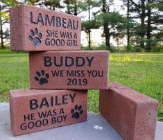 three bricks with names and paw prints are stacked on top of each other in the grass