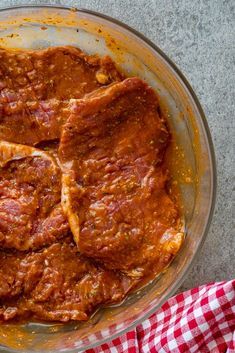 some meat is in a bowl on a table with red and white checkered cloth