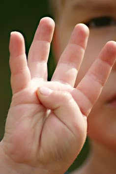 a young boy holding his hand up in the air with one hand and two fingers out