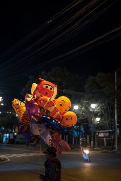 a man is walking down the street with many balloons in the shape of animals on his head