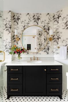 a bathroom with black and white wallpaper, gold accents and a round mirror above the sink