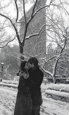 two people are kissing in the snow near a tree and bench on a snowy day