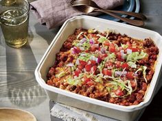 a casserole dish with meat and vegetables in it next to a glass of water