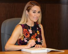 a woman sitting at a desk with a book in front of her and smiling for the camera