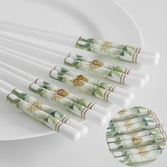 six white paper straws with green and yellow flowers on them next to a plate