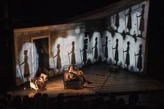 two people sitting on stage with shadows projected on the wall and behind them are chairs