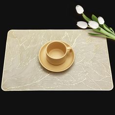 a cup and saucer sitting on top of a place mat with flowers in the background