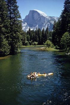 two people are floating on a raft in the middle of a river with mountains in the background