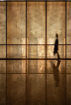 a person walking in front of a wall with many squares on it and the reflection of them