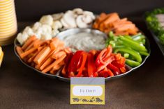 a plate with carrots, broccoli and other vegetables on it next to a jar of dip