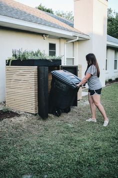 a woman is pushing a trash can out of the back yard