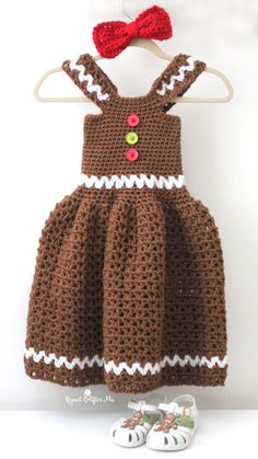 a crocheted brown dress and shoes are hanging on a clothes hanger with a red bow