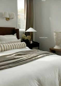 a bed with white sheets and pillows in a bedroom next to two lamps on either side of the bed