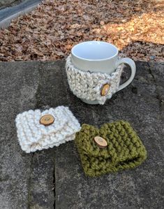 three crocheted items are sitting next to a coffee cup on a rock in the woods