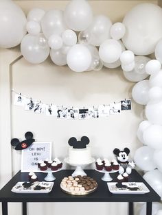 a table topped with cupcakes and cake next to white balloons in the shape of mickey mouse