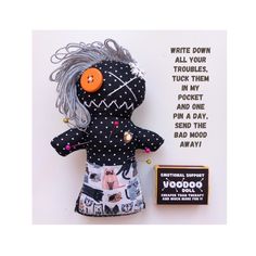 a black and white doll with an orange button on it's head next to a card