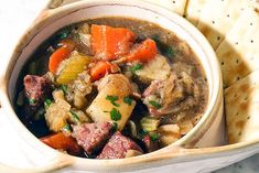 a bowl filled with stew next to crackers on a white counter top and bread