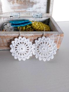 two white crochet doily earrings in a wooden box on top of a table