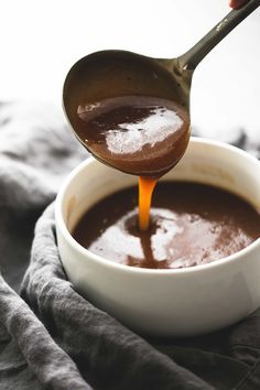 a spoon pouring chocolate into a white bowl on top of a gray cloth covered table