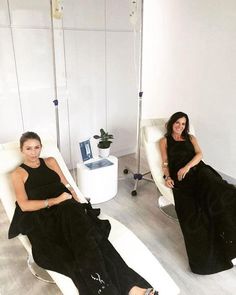 two women in black dresses sitting on white chairs