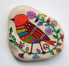 a rock with a bird painted on it and flowers around the edges, sitting on top of a white surface