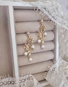 two pairs of earrings in a box on top of white lace and some other items