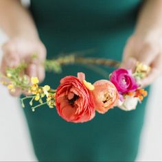 a woman holding flowers in her hands and wearing a green dress with yellow, pink, and red flowers on it