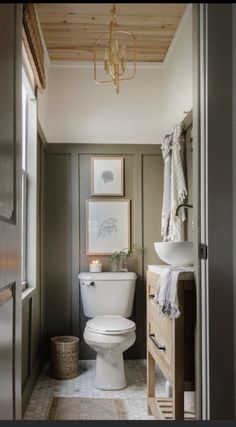 a white toilet sitting in a bathroom next to a sink and wooden cabinet under a chandelier