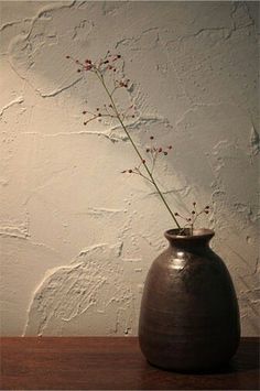 a vase with some flowers in it sitting on a table next to a white wall