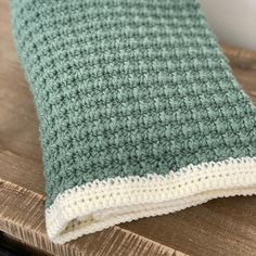 a green and white crocheted blanket sitting on top of a wooden table