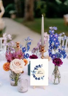 a table topped with vases filled with flowers next to a candle and greeting card