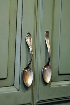 two spoons are hanging on the handles of green cabinets