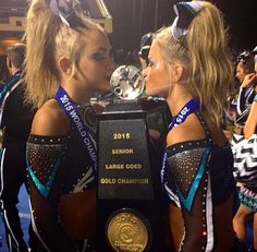 two cheerleaders kissing each other in front of a trophy