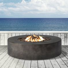 an outdoor fire pit sitting on top of a wooden deck next to the ocean and blue sky