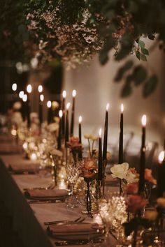 a long table is set with candles and flowers in vases on the tables, along with place settings