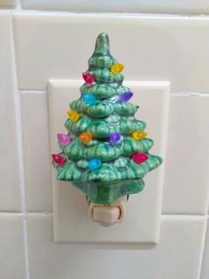 a green christmas tree light switch cover on a white tile wall with colorful lights around it