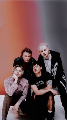 three young men sitting next to each other in front of a rainbow colored wall and posing for the camera