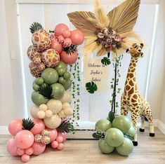 a giraffe and balloon arch in front of a window with greenery on it