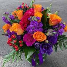 a vase filled with lots of colorful flowers on top of a cement floor next to a parking lot