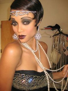 a woman in a black dress with pearls on her head and necklaces around her neck