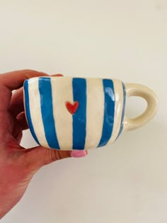 a hand holding a blue and white striped coffee cup with a heart painted on it